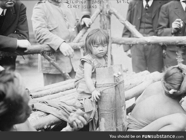 1906 photo of a young Filipino girl sitting on a wooden bench in a human zoo enclosure in