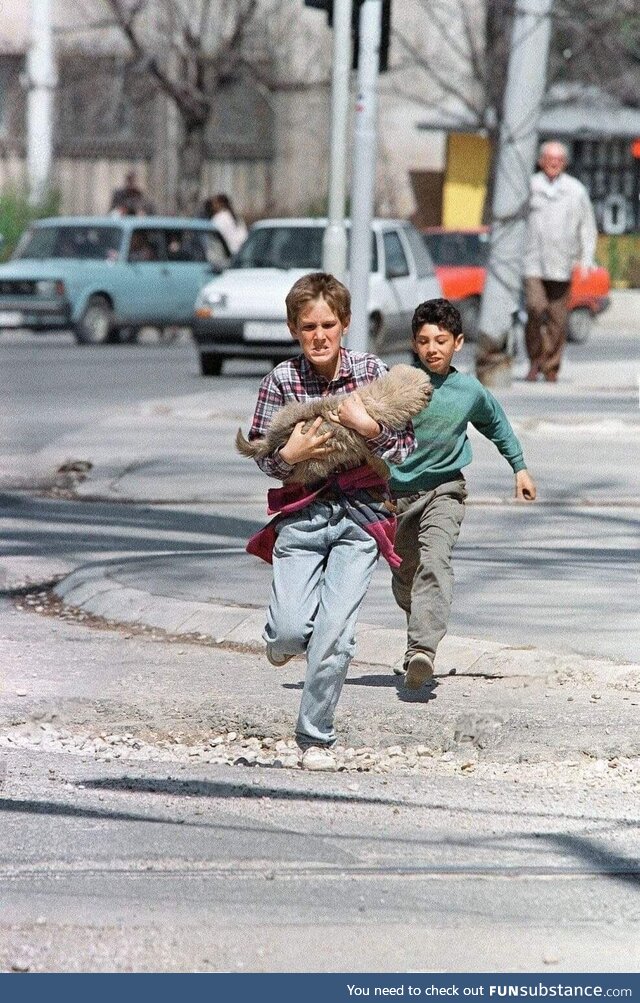 A boy carrying his dog while crossing the infamous “Sniper Alley” - April 1995