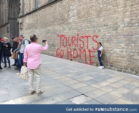Tourists taking a picture in front of a "Tourists go home" graffiti in Barcelona