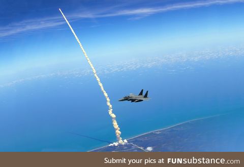 An F-15E patrols Kennedy Space Center as the Space Shuttle Atlantis launches