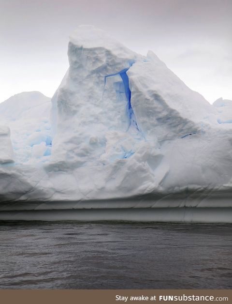 A bright brilliant blue glows from within an Antarctic iceberg