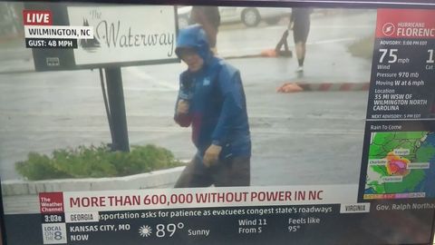 Reporter plays up the hurricane while two dudes casually walk in the background