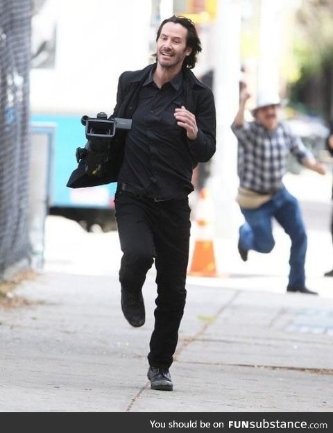 A photo of Keanu Reeves running away with a camera he took from a Paparazzi guy is