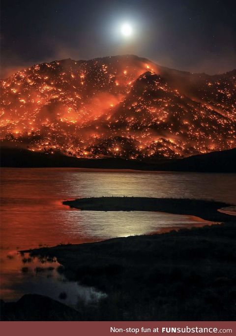 The moon rises above a mountain in California completely covered in wildfires