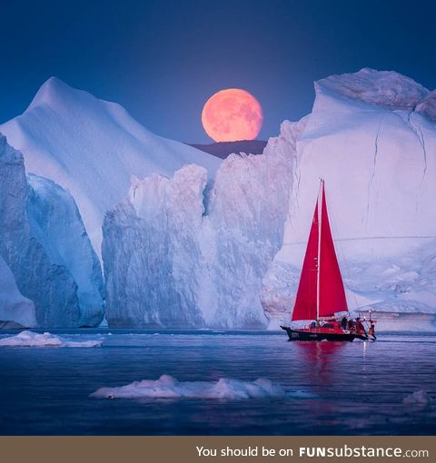 A sailboat passing under a blood moon in Greenland