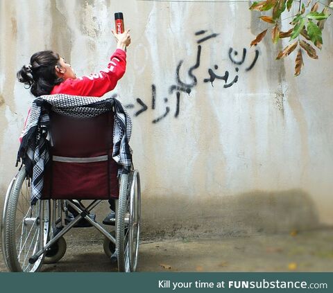 Brave woman with disability writing "Woman, Life, Freedom" on a wall in Sanandaj, Iran -