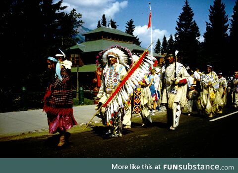 Procession of First Nations people passing tourists somewhere in Canada (BC, perhaps) c